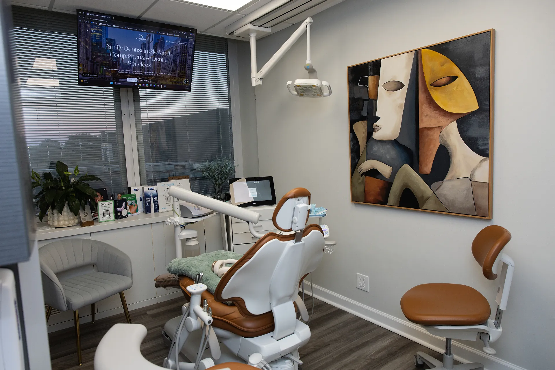 Dental treatment room with brown dental chair, abstract painting, and overhead monitor — My Dental Hub in Skokie, IL