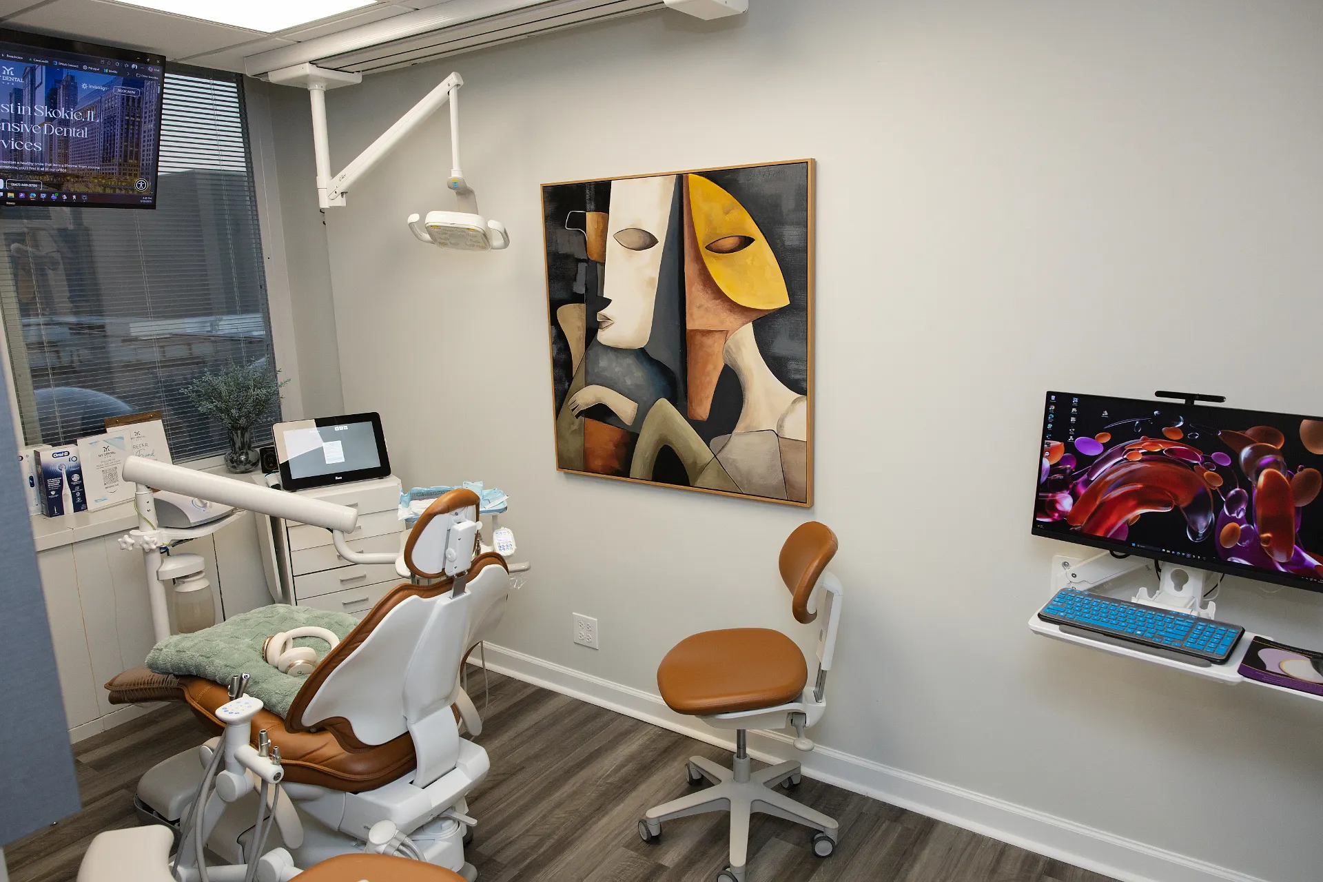 Dental operatory with a brown and white treatment chair, matching dentist stool, abstract art on the wall, and computer workstation — My Dental Hub in Skokie, IL