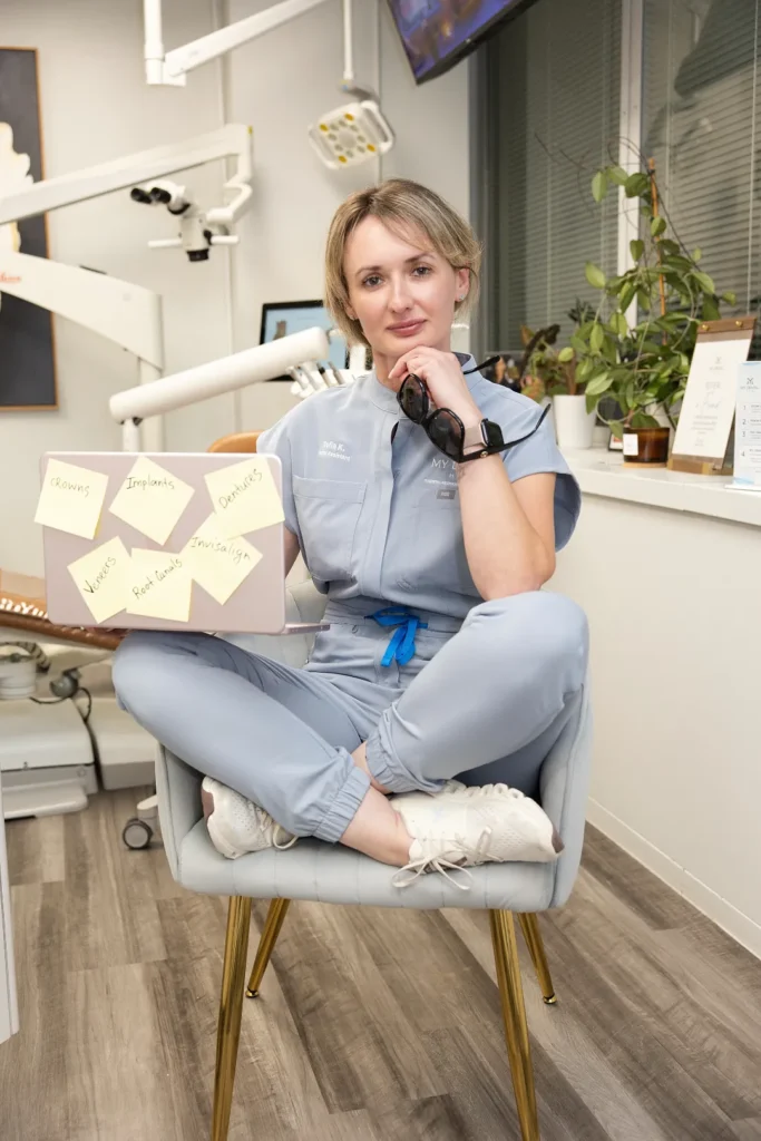 Adult female staff member sitting cross-legged in a chair holding a laptop with sticky notes — My Dental Hub in Skokie, IL