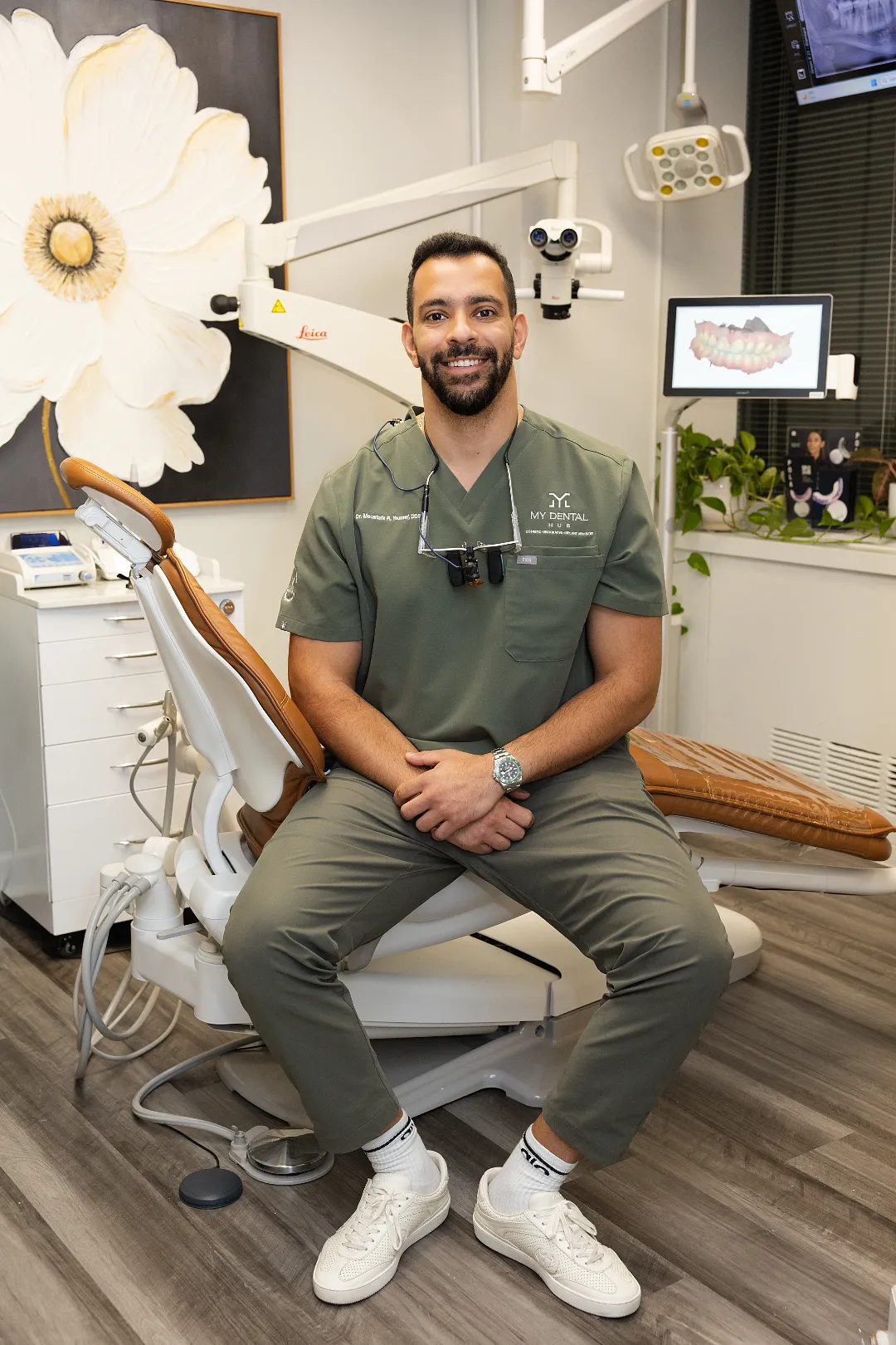 Adult male dentist in green scrubs smiling while seated on a dental chair in an operatory — My Dental Hub in Skokie, IL