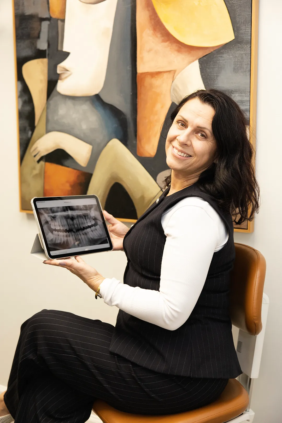 Female staff member holding a tablet showing dental x-rays in front of abstract artwork — My Dental Hub in Skokie, IL