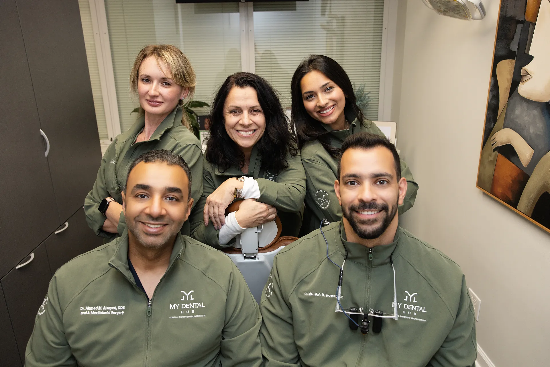 Five dental team members in matching green jackets smiling together in an office — My Dental Hub in Skokie, IL